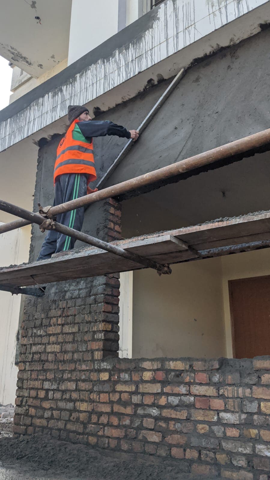 Worker plastering a balcony soffit from scaffolding